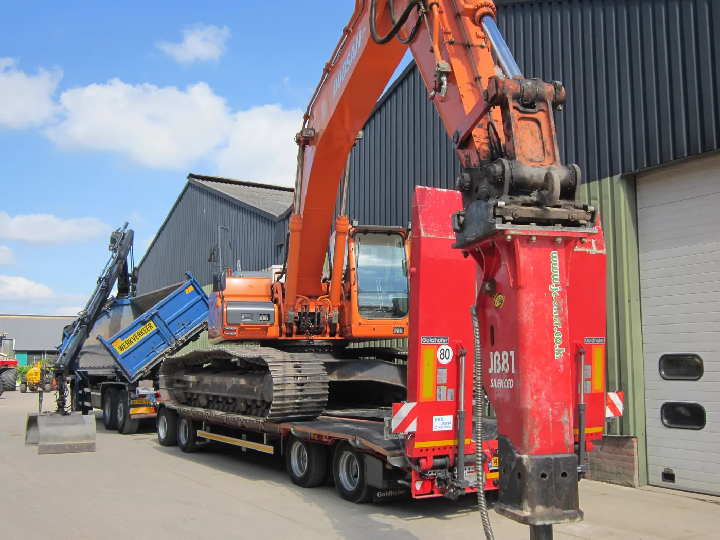 Oranje graafmachine op een dieplader bij een loods